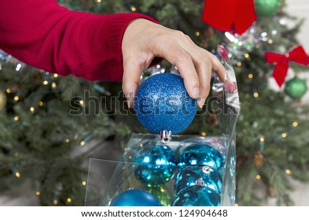 Female hand putting away holiday ornaments to end the season with Christmas tree in background