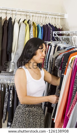 Vertical portrait of mature Asian woman selecting clothes while dressing in walk-in closet