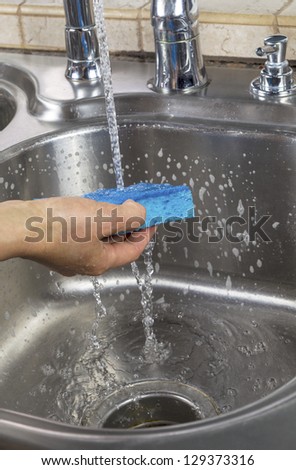 Vertical photo of female hand rinsing soapy sponge with water running out of faucet