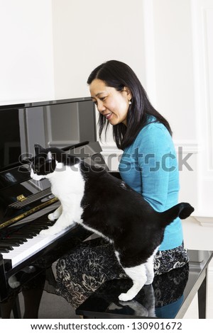 Vertical photo of mature woman watching her family cat with his paws on the keyboard of the piano