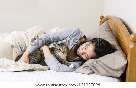 Horizontal photo of mature woman, lying head down in pillow, while hold her family cat in bed
