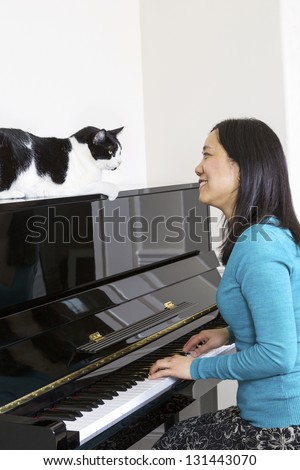 Vertical photo of mature woman with her family cat on top of piano looking at each other while sitting at the piano