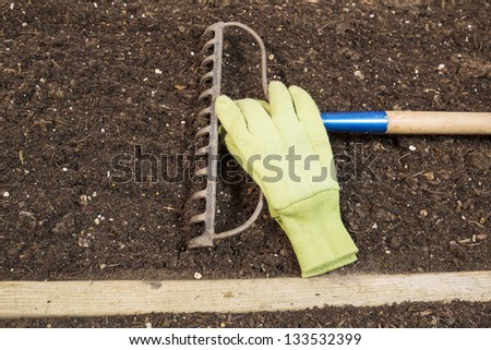 Horizontal photo of garden rake in soil with work gloves next to rake Teeth