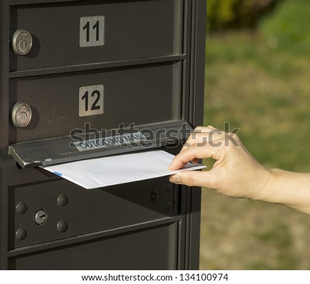 photo of female hand putting letter into outgoing postal mailbox with green grass in background