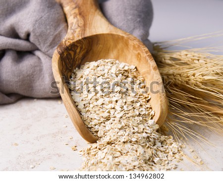 Horizontal photo of rolled oats in wooden spoon with cloth napkin and wheat stalks on natural white stone