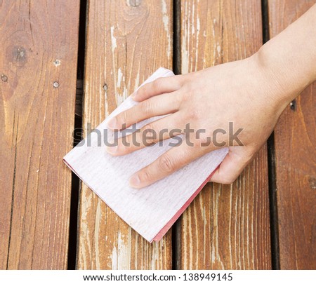 Photo of female hand with sand paper on natural faded cedar wood deck