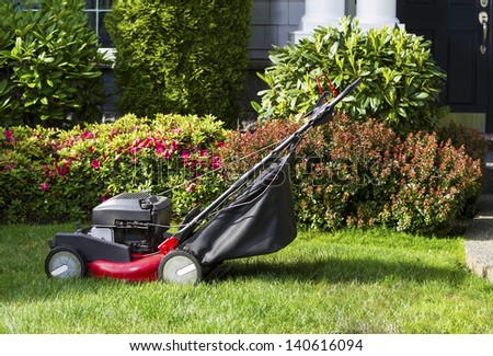 Horizontal photo of old gas lawnmower on front yard with home in background
