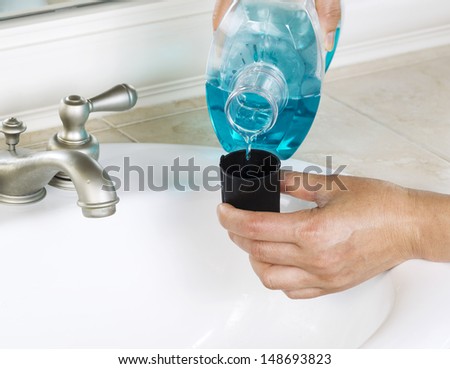 Horizontal Photo Of Female Hands Putting Mouth Wash Into Black Cap With White Bathroom Sink And Faucet In Background