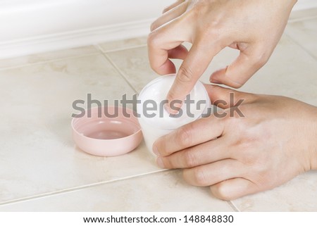 Close up horizontal photo front of female index finger dipping into cosmetic cream