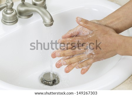 Horizontal photo of female hands rinsing soap off with running water and bathroom sink in background