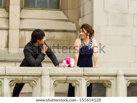 Horizontal Photo of young adult man looking at his lady friend, bouquet of flowers between them, with building in background