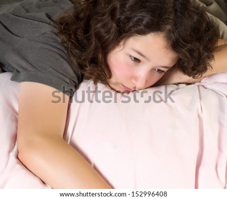Young girl trying to wake up in the morning with her eyes open while lying in a messy bed