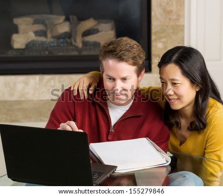 Photo of close mature couple looking at information on the computer screen together with fireplace in background