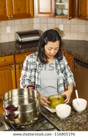 Vertical photo of mature woman working with cooked winter melon on dinner plate next to cooking kettle on stove top