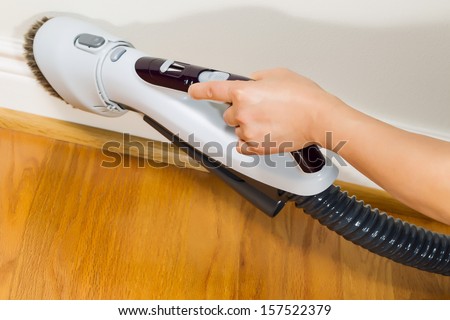Horizontal photo of female hand with vacuum cleaner brush extension cleaning trim work near wooden floors