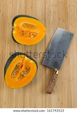 Vertical photo of half cut large acorn squash with butcher knife on natural bamboo cutting board