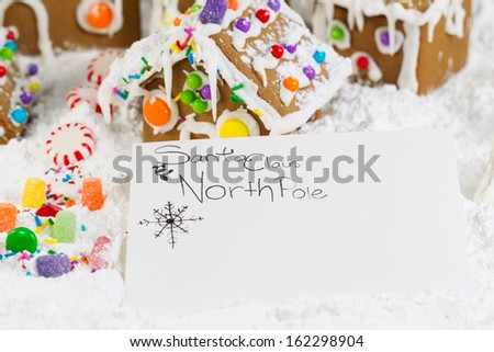 Closeup horizontal photo of letter to Santa with Gingerbread houses, surrounded by powdered snow in background
