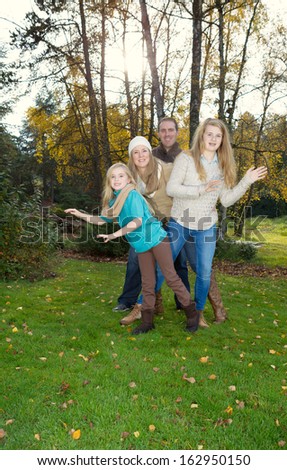Vertical photo of family dancing in front of trees, with sunlight coming through, during a nice day in the fall season