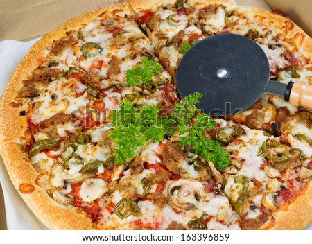 Photo of fresh pizza topped with parsley, mushroom, and peppers in a box with cutter on top