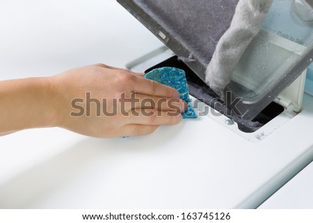 Horizontal photo of female hand with sponge removing lent from dirty air filter out of dyer machine