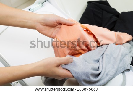 Photo of female hands taking the dry laundry out of the dyer