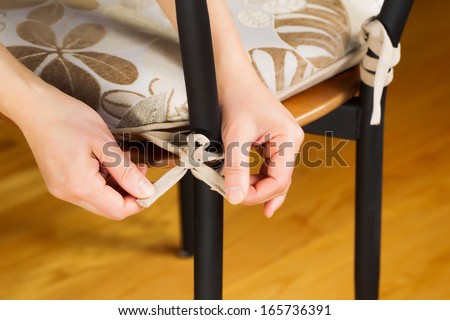 Horizontal photo of female hands tying knot on chair seat cushion with Oak wooden floors in background