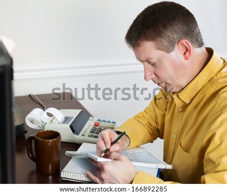 Photo of mature man, recording data from the computer, working on his taxes with tax booklet and pencil in hands