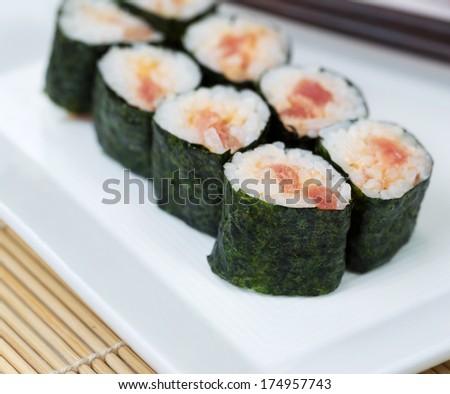 Closeup photo of freshly made spicy tuna sushi roll in white plate and chop sticks in background with bamboo mat underneath
