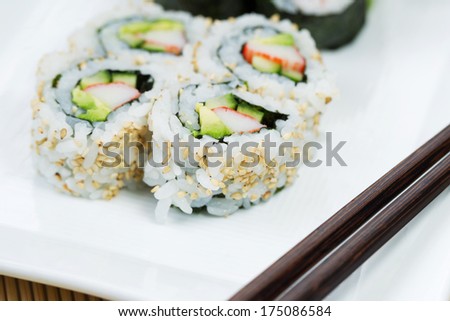 Closeup horizontal photo of freshly handmade California sushi rolls in white plate and chop sticks in forefront with bamboo mat underneath