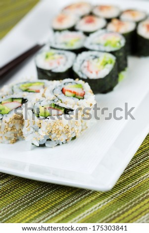 Closeup vertical photo of freshly handmade sushi rolls, filling white plate, and chop sticks in background with texture green cloth underneath