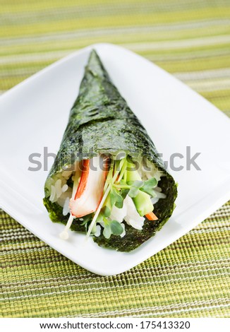 Closeup vertical photo of freshly handmade Temaki sushi cone in white plate with textured green cloth mat underneath