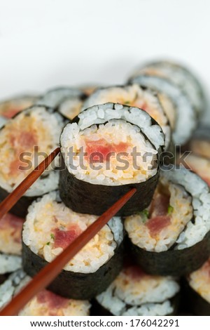 Closeup vertical photo of a single spicy tuna roll on top of sushi stack being picked up with chopsticks