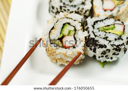 Closeup horizontal photo of a single inside out California roll being picked up with chopsticks