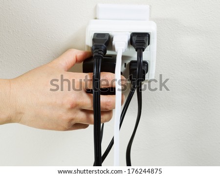 Photo of female hand plugging in power adapter into multiple electrical wall unit outlets