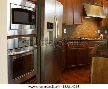 Closeup photo of a stainless steel appliances in modern residential kitchen with stone counter tops and cherry wood cabinets with hardwood floors