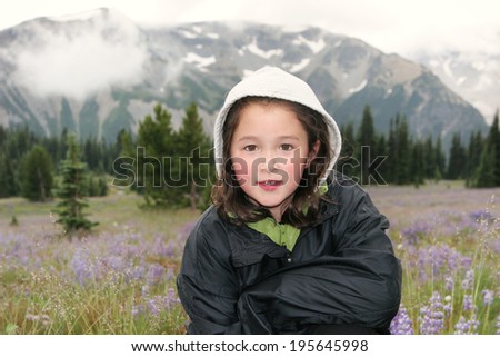 Horizontal photo of young girl, looking forward, during early spring with mountains and wild flowers in background