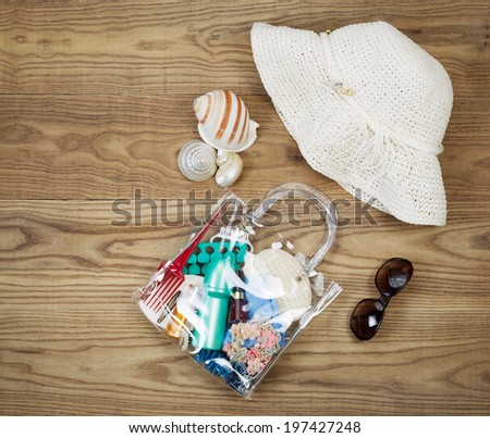 Overhead view of outdoor kit placed on rustic wooden boards.  Items include clear plastic bag, comb, sun screen, hair clips, sea shells, sun glasses and white hat.