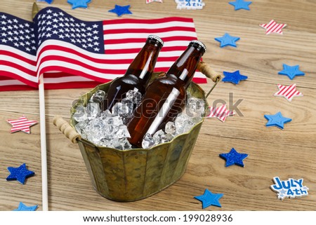 Horizontal photo of glass bottled beer in old metal bucket filled with ice and American flags in background for celebration of Independence Day