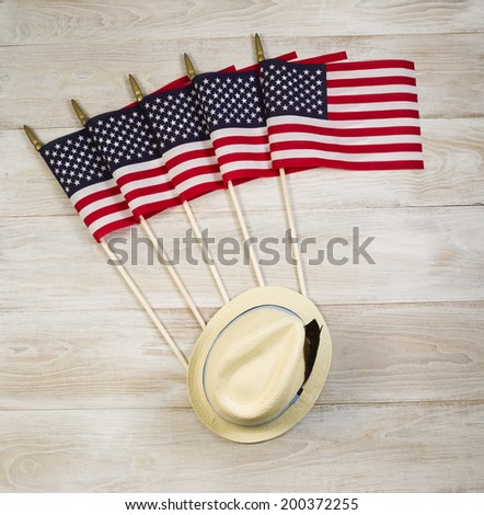 Overhead view of five United States of America flags and hat placed on faded white wood.