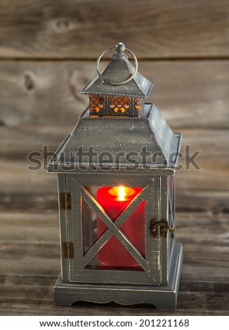 Vertical front view of an old Asian design lantern with red candle burning brightly inside on rustic wood