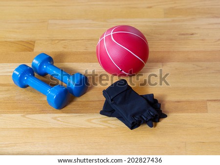 Workout gloves, dumbbells and weight ball lying on wooden gym floor