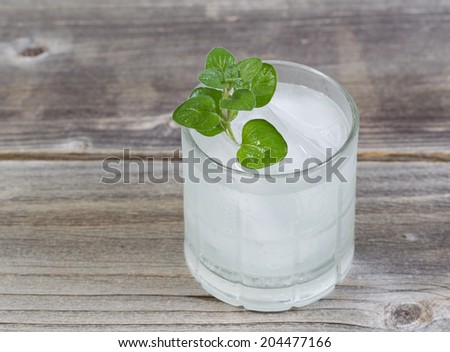 Closeup top view of a fresh cold drink with seasonal mint on top with ice in glass on rustic wood