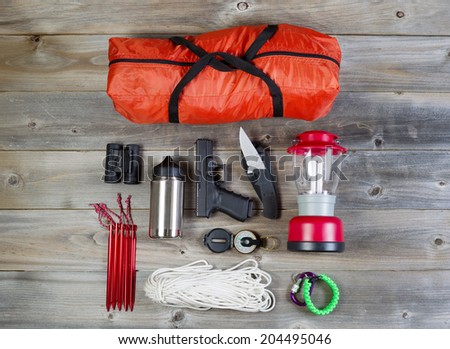 Overhead view of hiking gear and personal protection, pistol and knife, placed on rustic wood