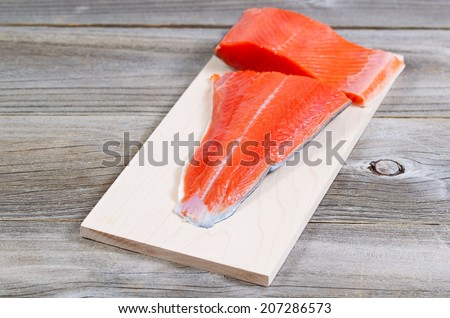 Closeup horizontal front view of raw red salmon, skin side down, on maple wood grilling plank with rustic wooden boards underneath