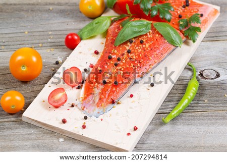 Closeup horizontal front view of raw red salmon, skin side down, on maple wood grilling plank with seasoning and other herbs