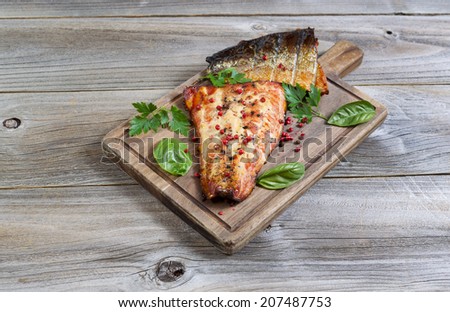 Horizontal view of smoked salmon fillets, fresh out of cooker, with seasoning on serving board with rustic wood underneath