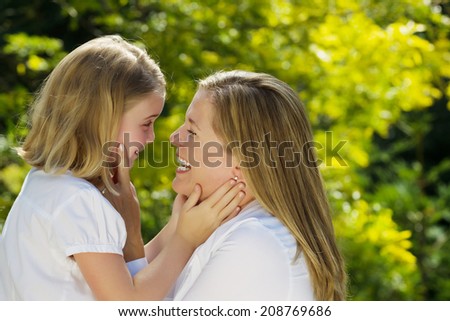 Side view of mother looking into the eyes of her youngest daughter while holding her face in her hands during outing outdoors on patio with blurred out woods in background