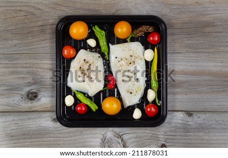 Top view of fresh raw Cod Fish Fillets in cooking pan with tomatoes, garlic, peppers and peppercorn salt on rustic wooden boards