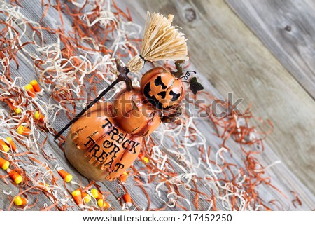 Horizontal angled image of a scary orange pumpkin figure holding straw broom placed on rustic wooden boards