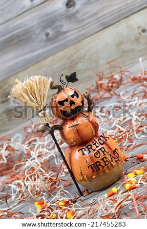Vertical angled image of a scary orange pumpkin figure holding straw broom placed on rustic wooden boards